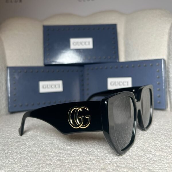 Black oversized geometric sunglasses, angled view showing the wide gold logo temple